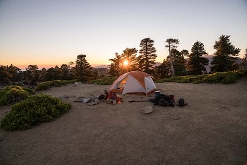 A pitched tent in nature, with the sun setting in the distance